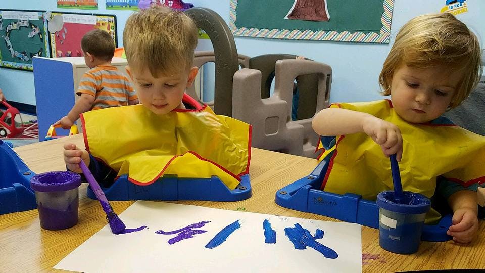 Two children painting with brushes and paint pots in a classroom