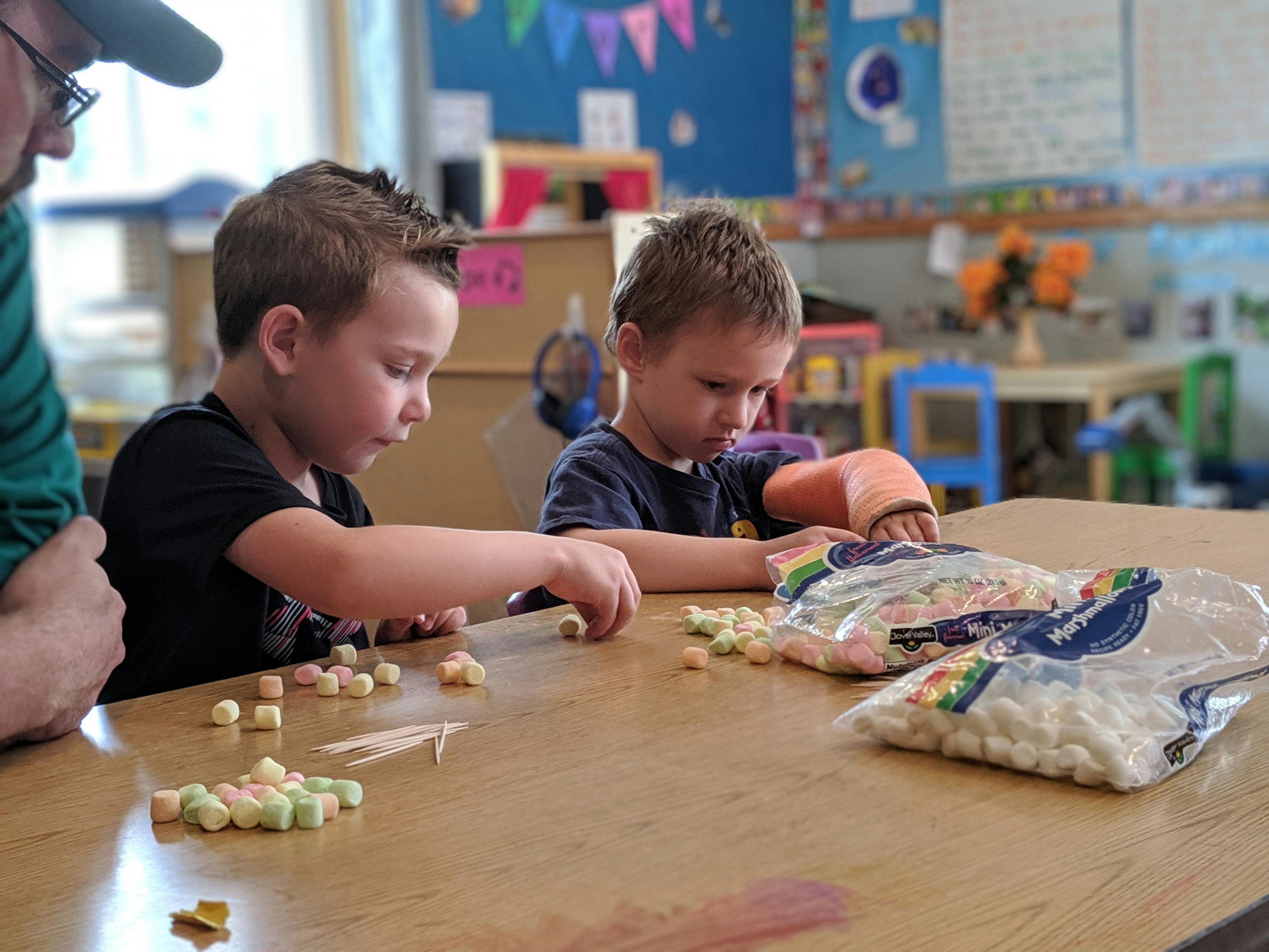 Two children playing with marshmallows and toothpicks at a table