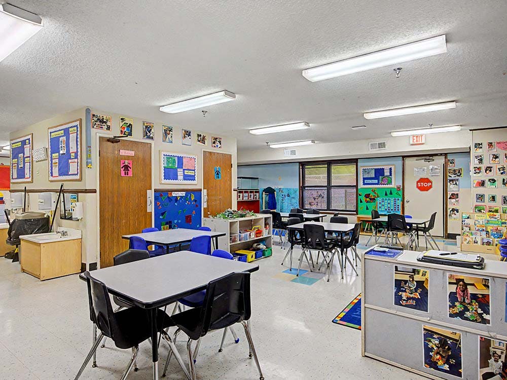 Classroom with small tables and chairs arranged, bulletin boards on walls