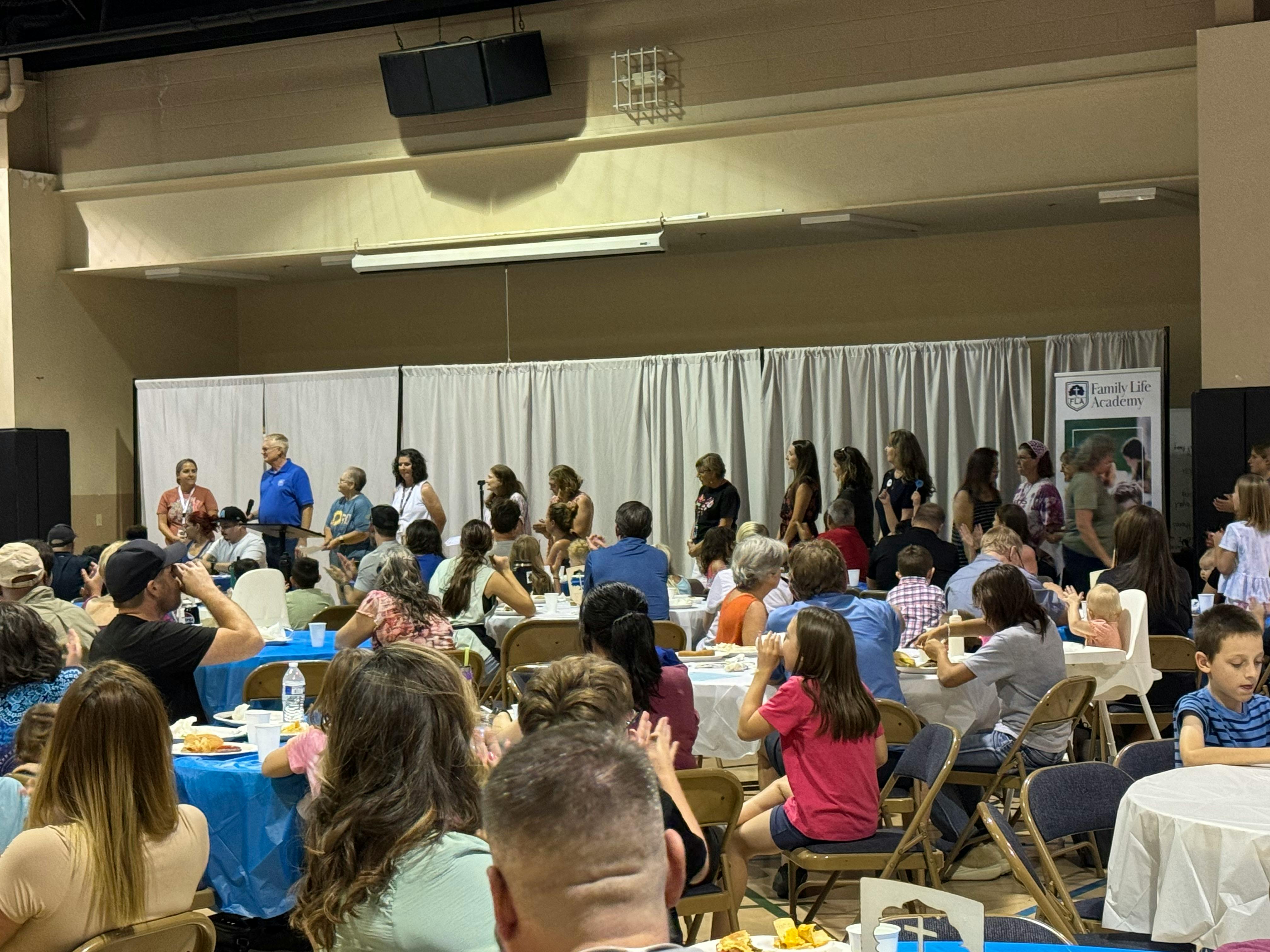 People gathered in a large room, some seated at tables, others standing