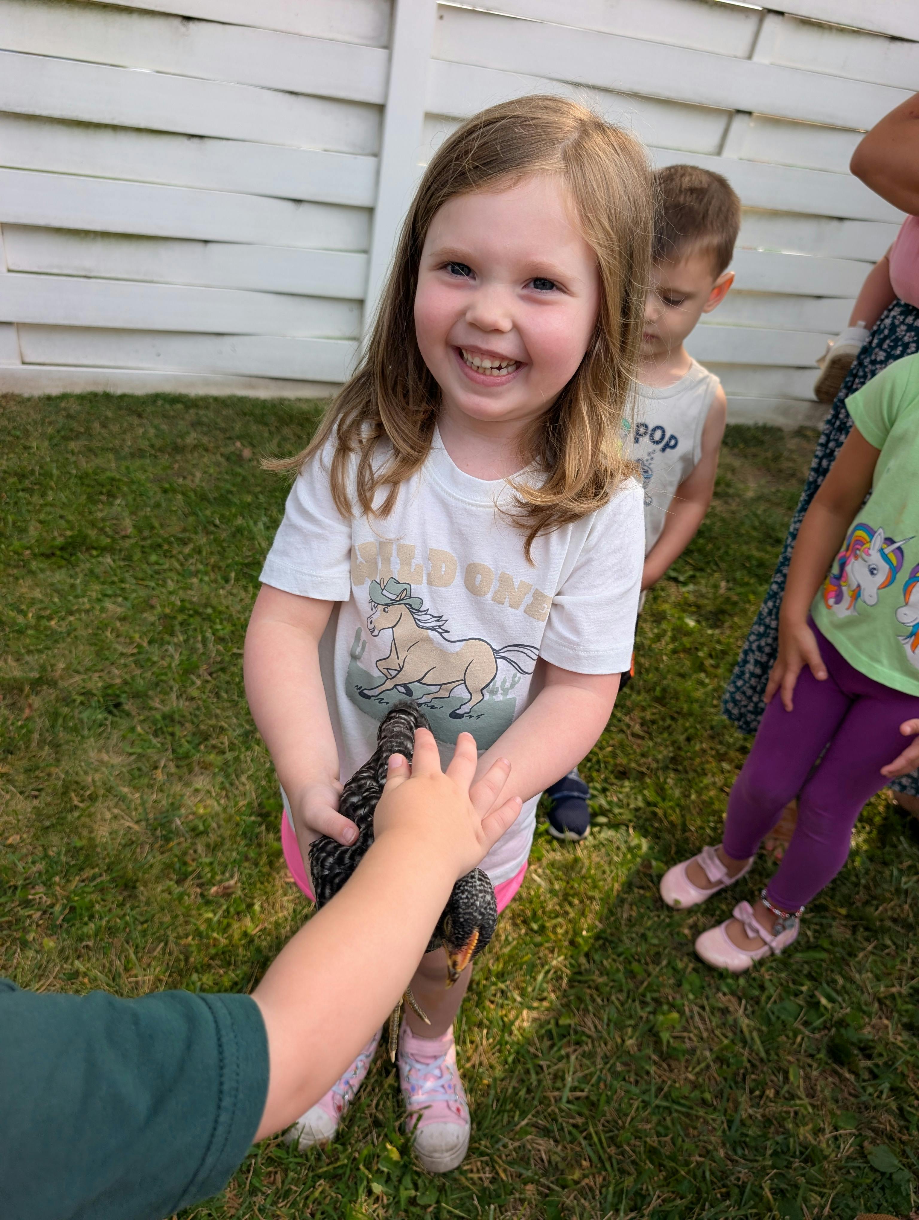 Child holding a chicken while another child reaches out to pet it