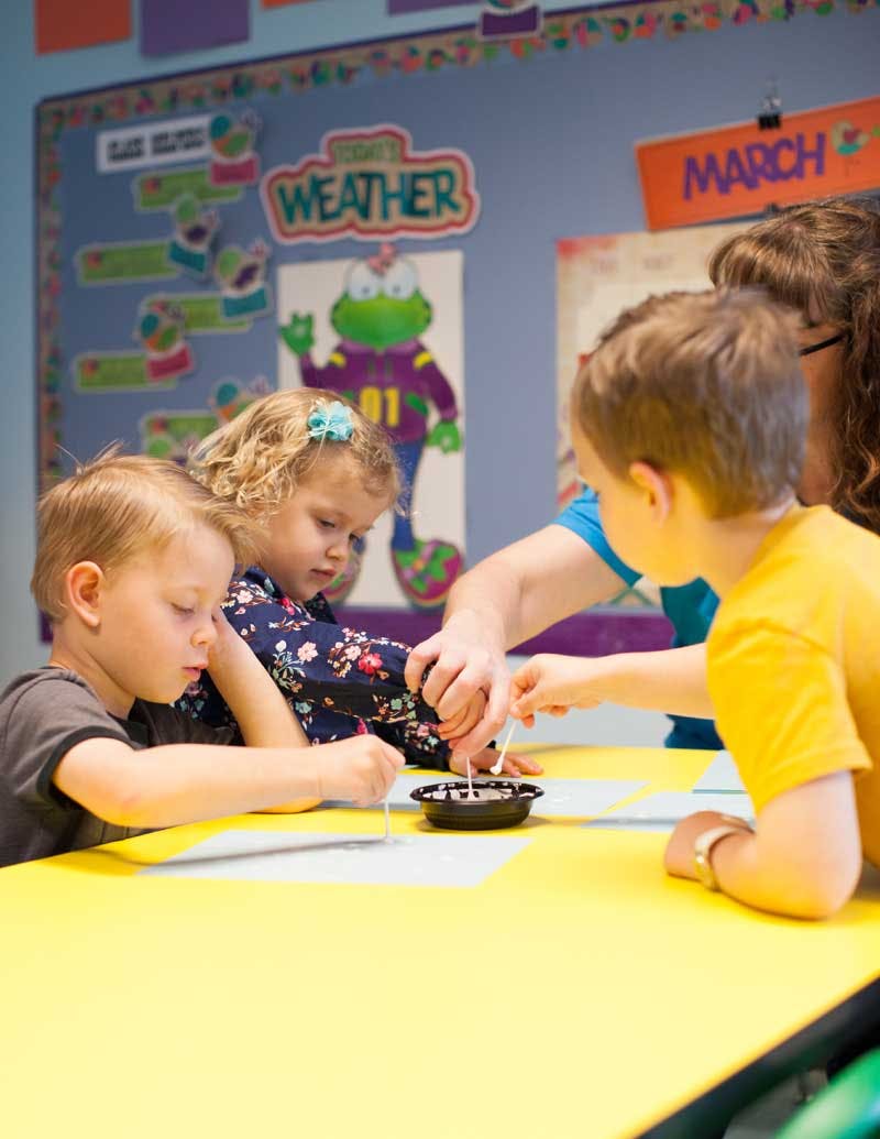 Adult and two children doing an activity at a table in a classroom