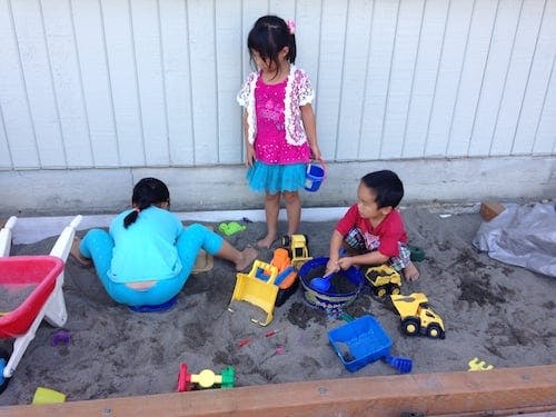Three children playing in a sandbox with toys