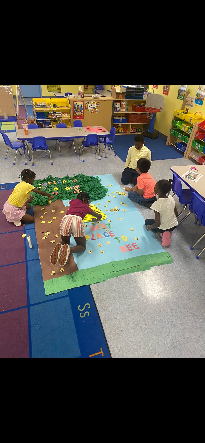 Adult and children on floor working on a large craft project in a classroom