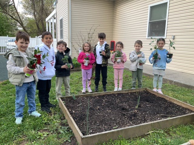 Group of children holding potted plants next to a garden bed