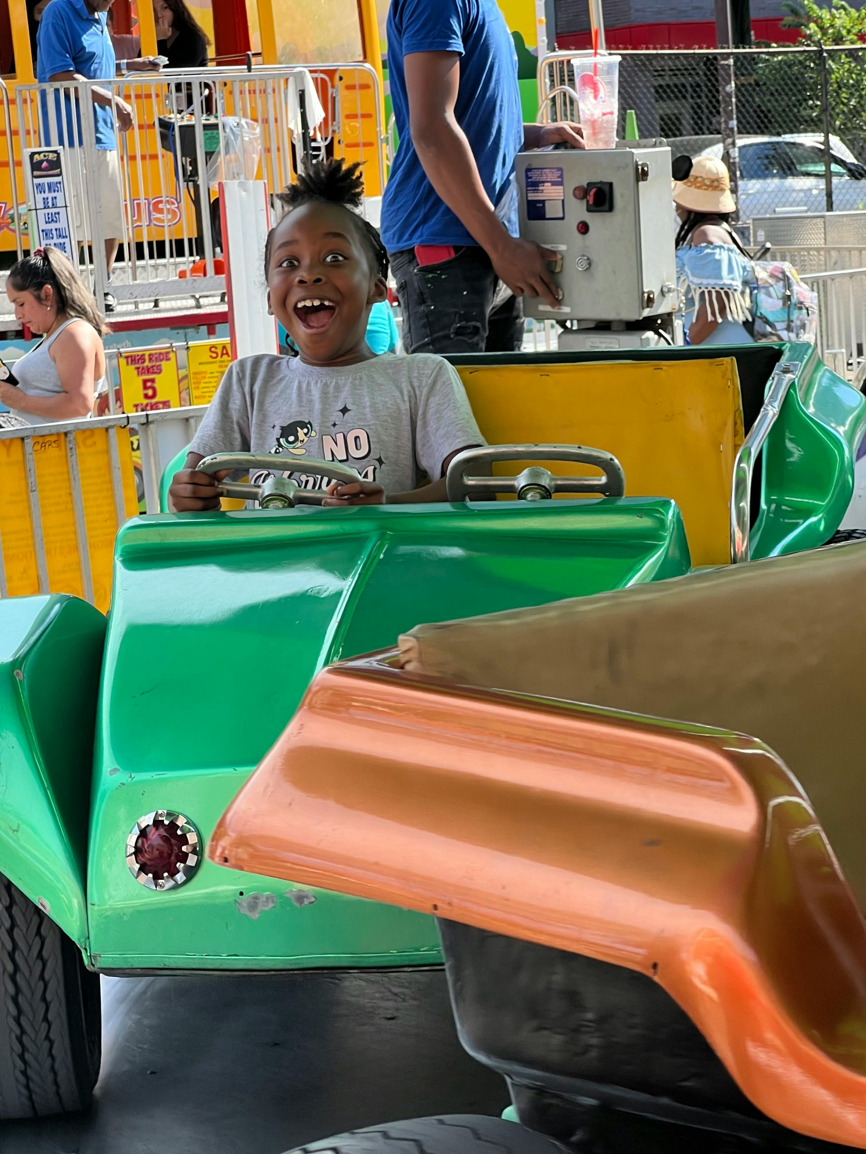 Child in a green ride car with mouth open
