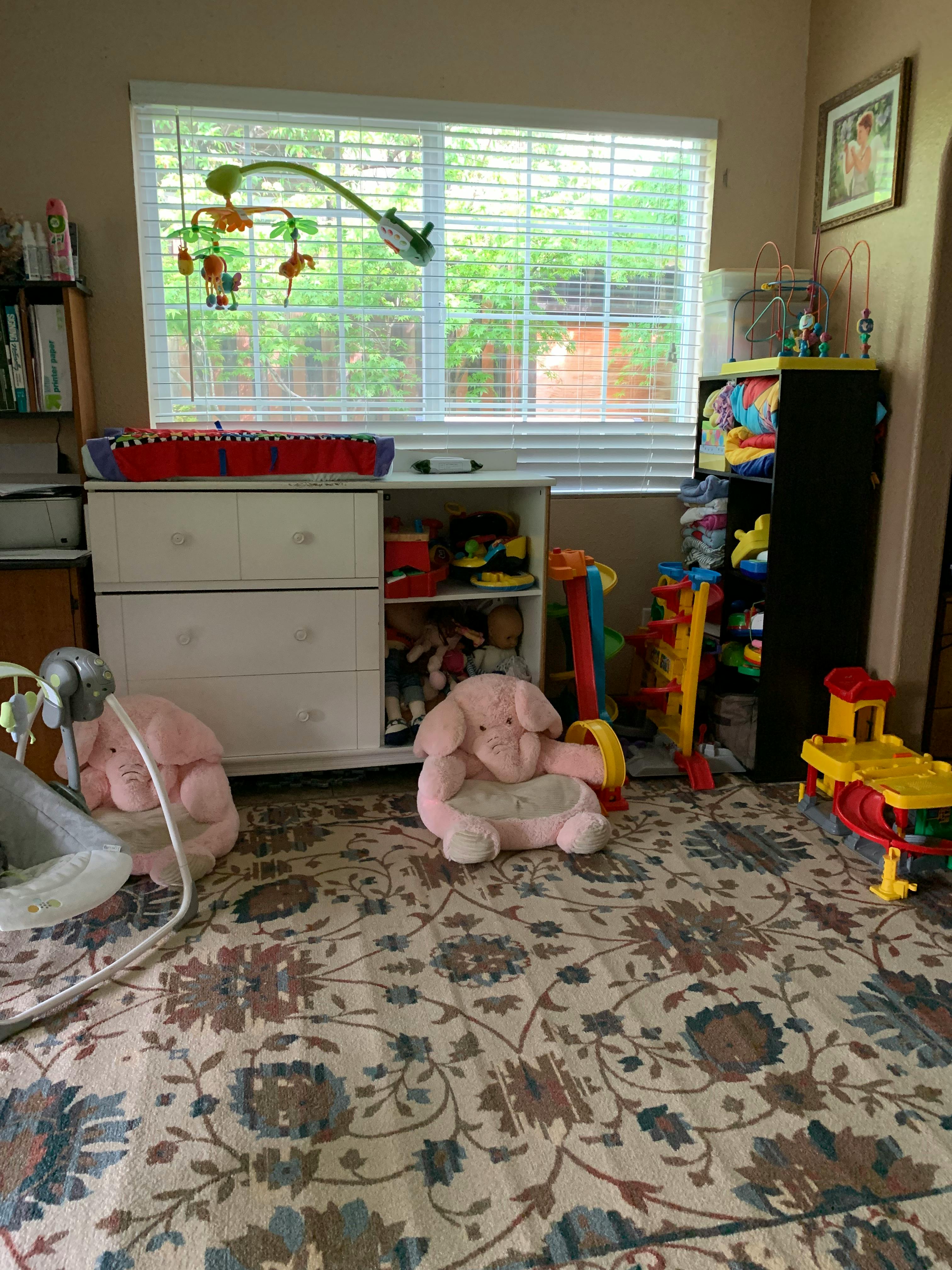 Nursery room with a window, dresser, and toys on a patterned rug