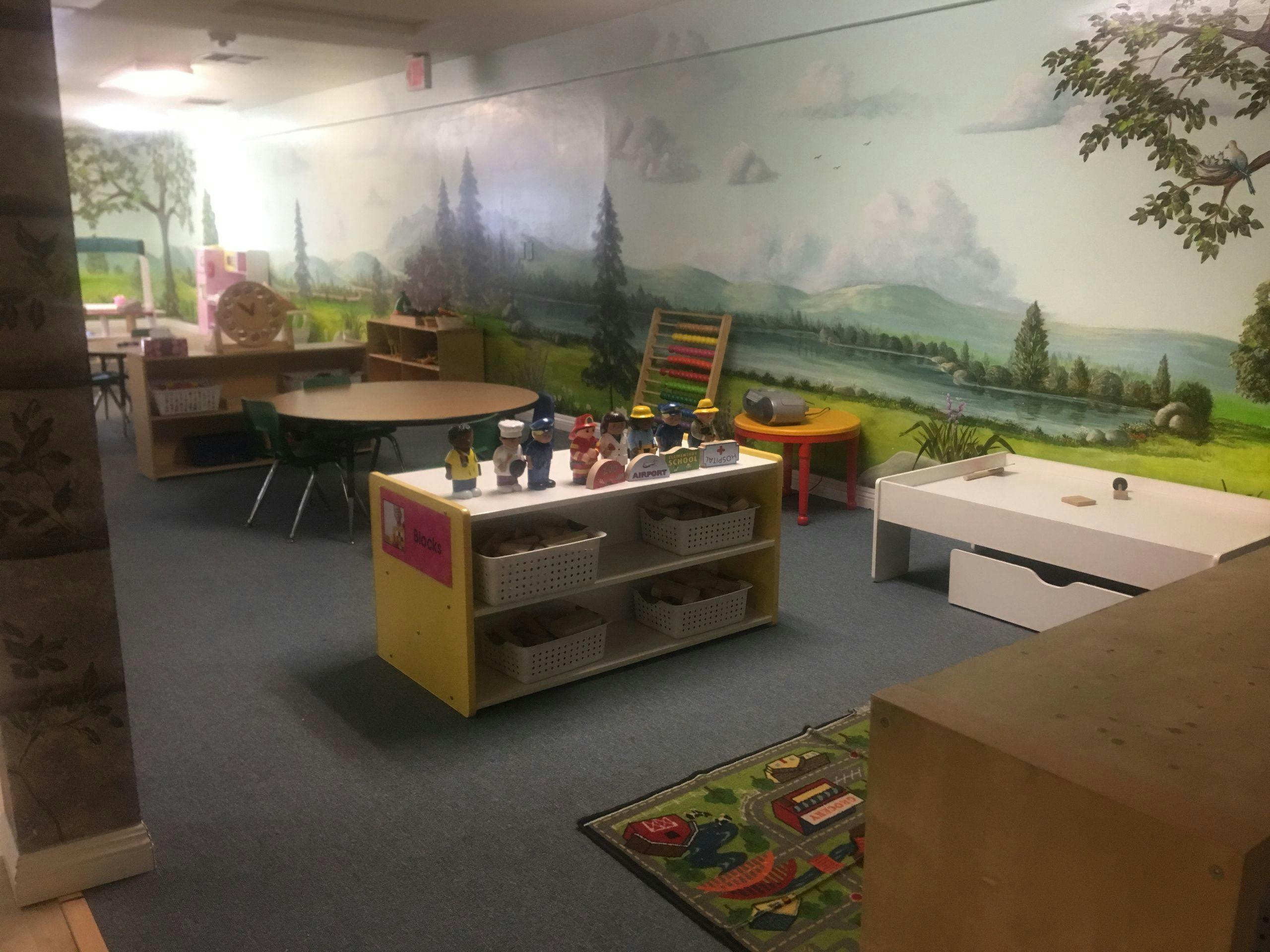 Playroom with tables, shelves, and a nature mural on the wall