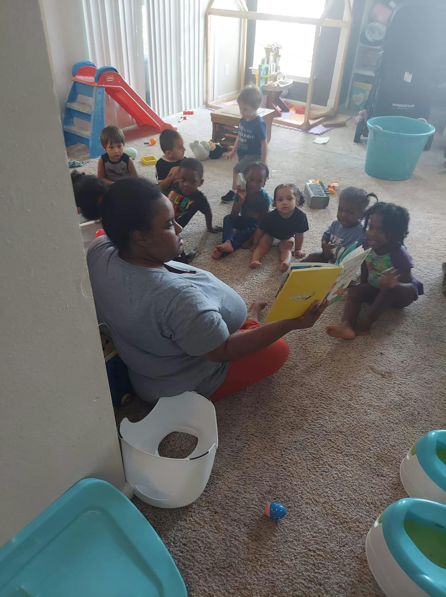Person reading a book to a group of children sitting on the floor