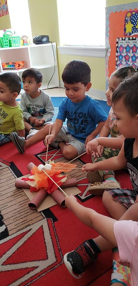 Children sitting on a rug playing with a craft campfire and sticks