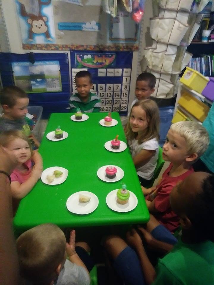 Children sitting around a green table with cupcakes
