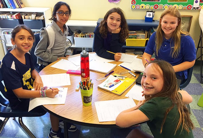 Five children studying together at a round table in a classroom