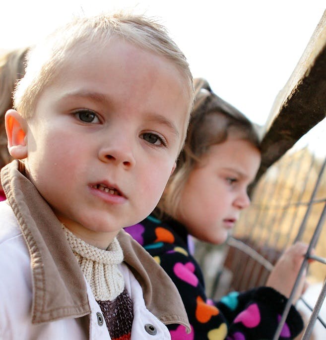 Child in foreground, another child in background looking at a fence