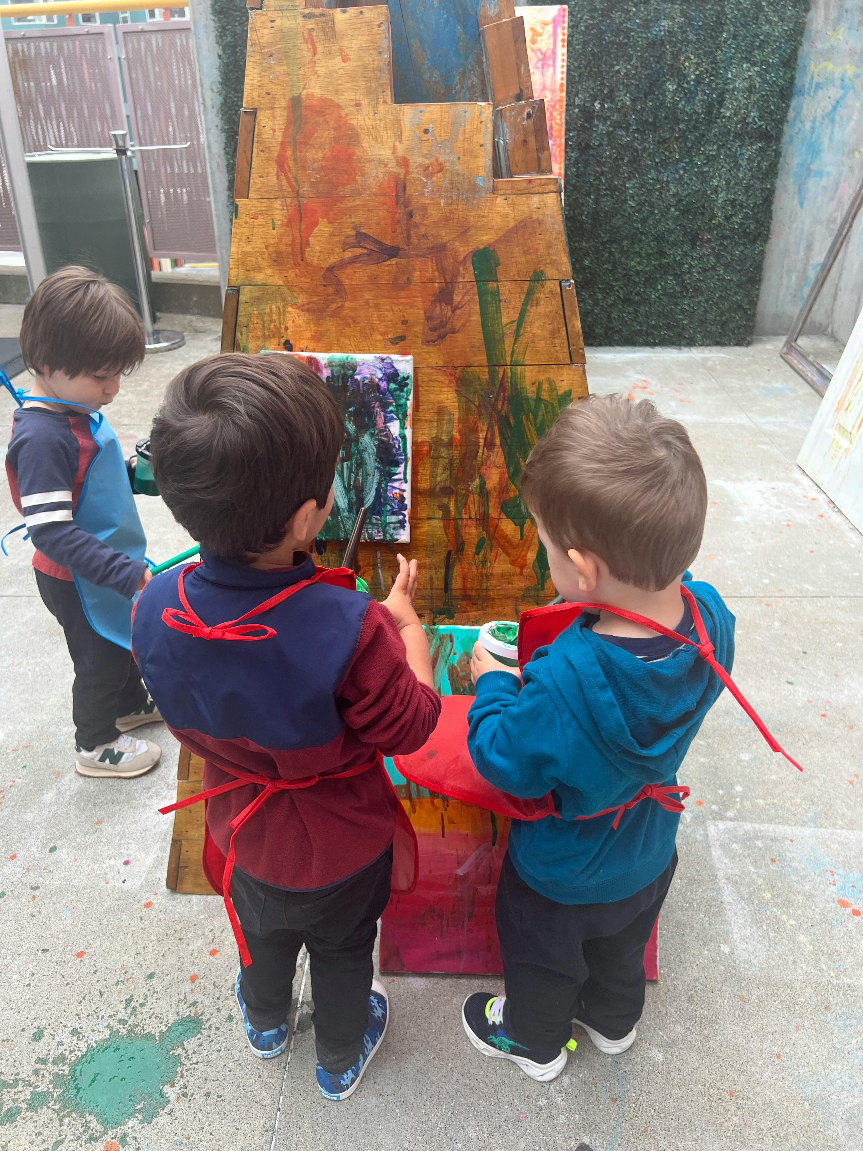 Three children painting on an easel outdoors