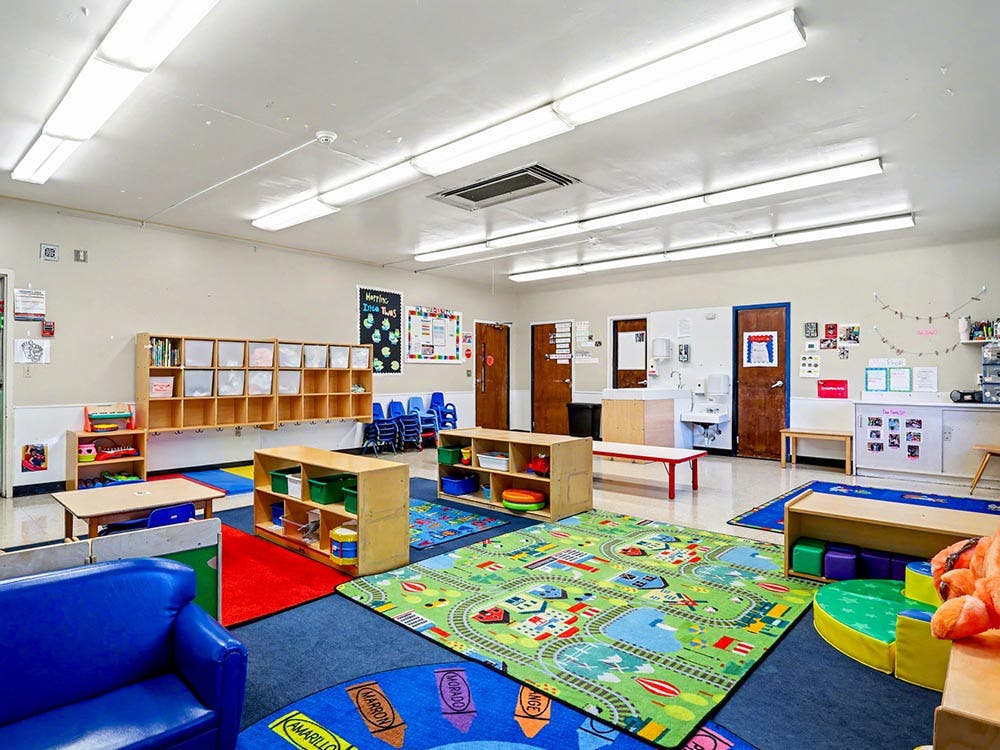 Colorful classroom with play rugs, cubbies, small tables, and sinks
