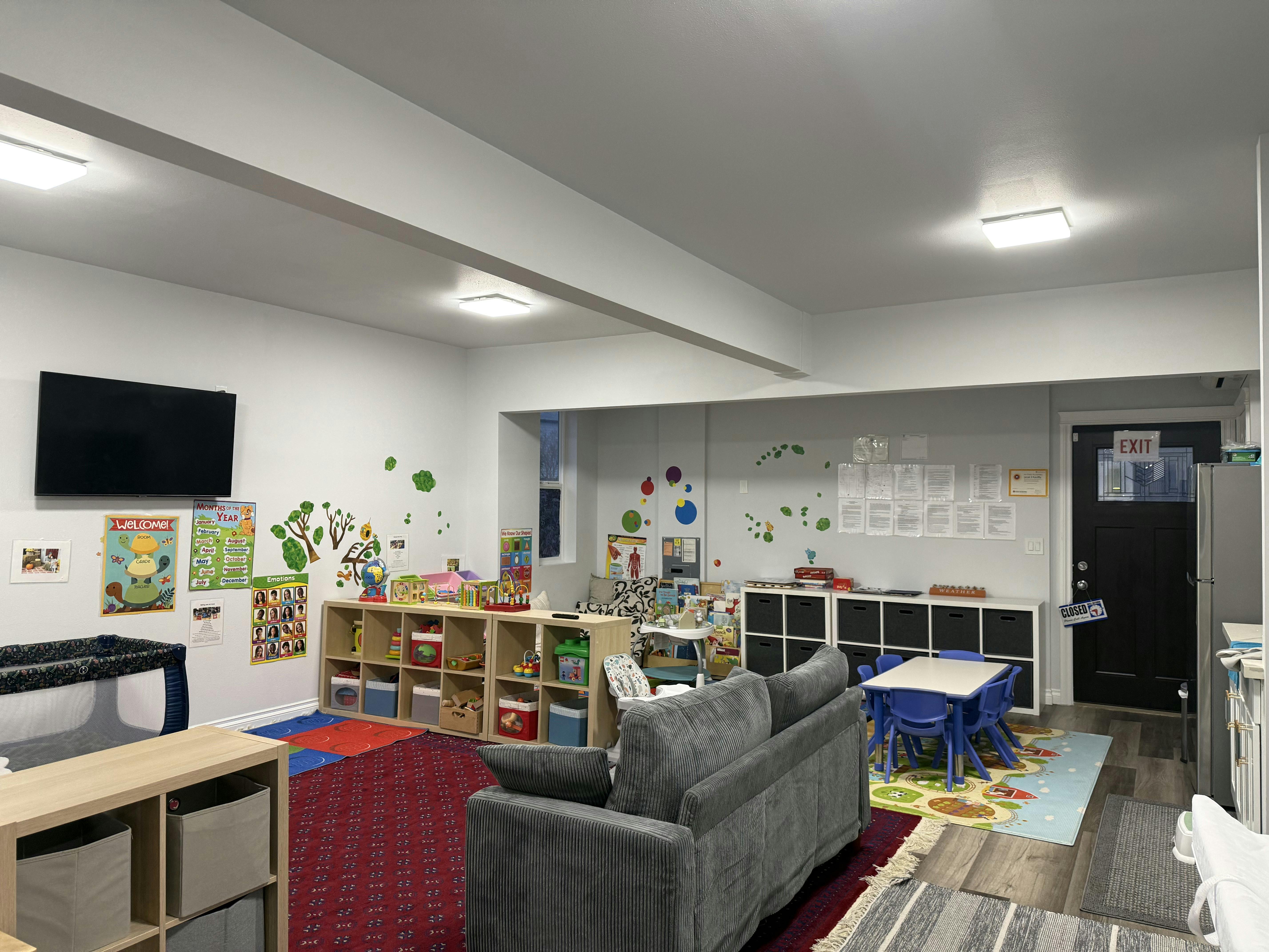 Childcare playroom with educational posters, toys, small tables, and a grey sofa