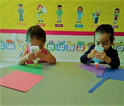 Two children using glue bottles at a table with construction paper
