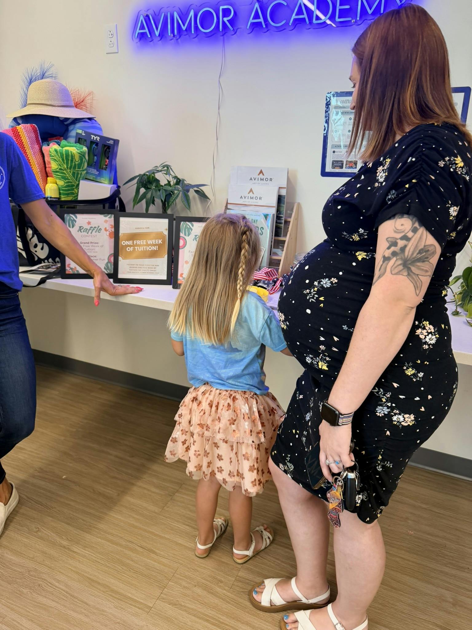 Pregnant person standing next to a child looking at a desk with raffle signs