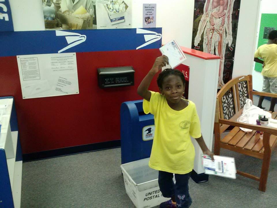 Child holding up a letter next to a mailbox