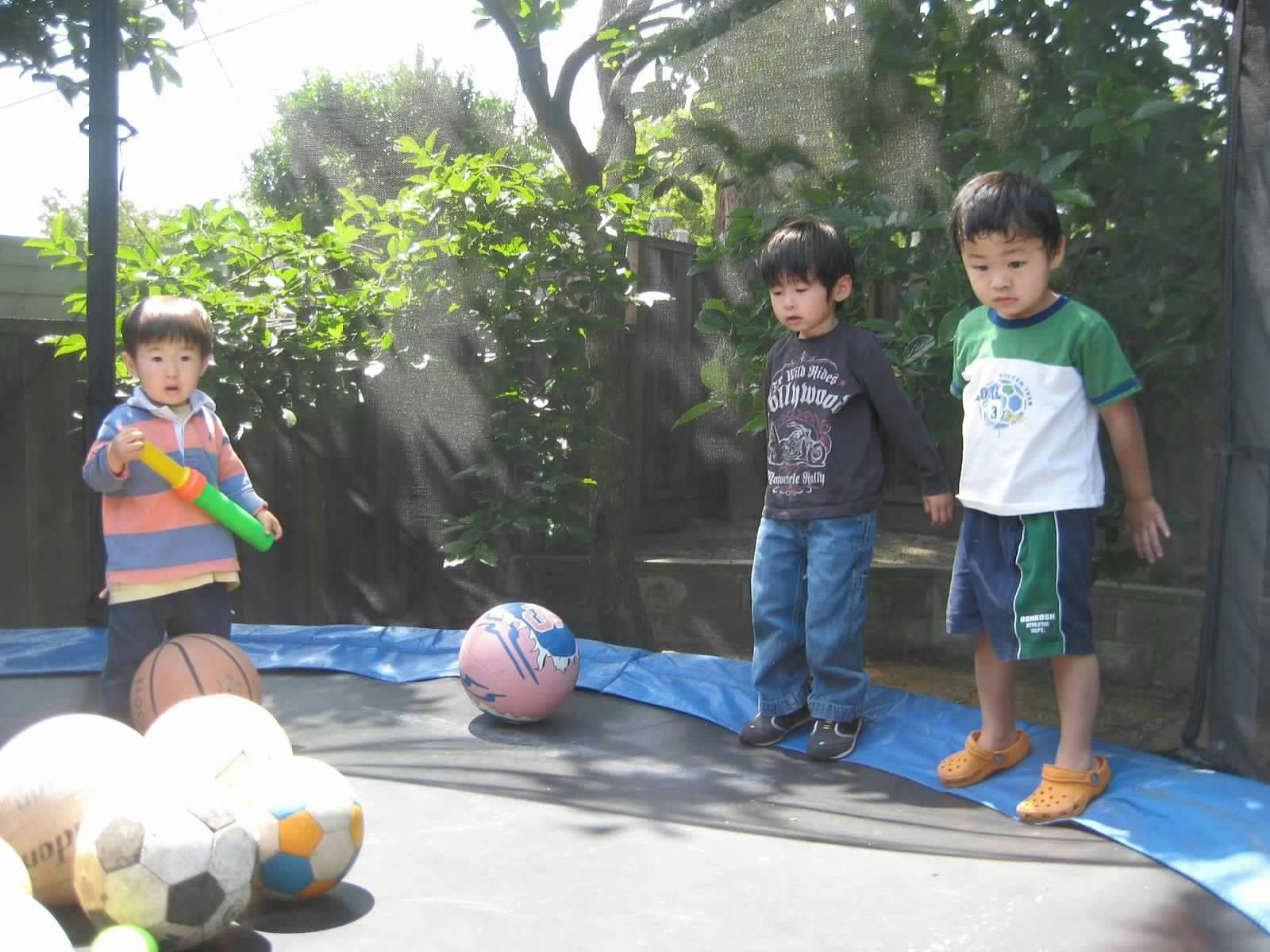 Three children standing on a trampoline with several balls