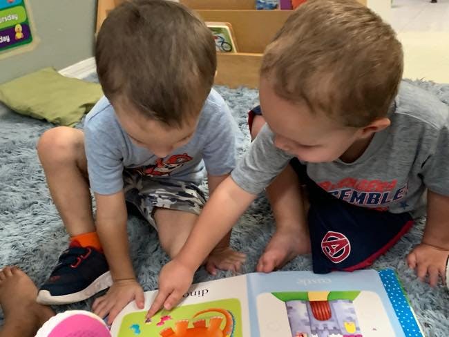 Two children sitting on a rug looking at a book