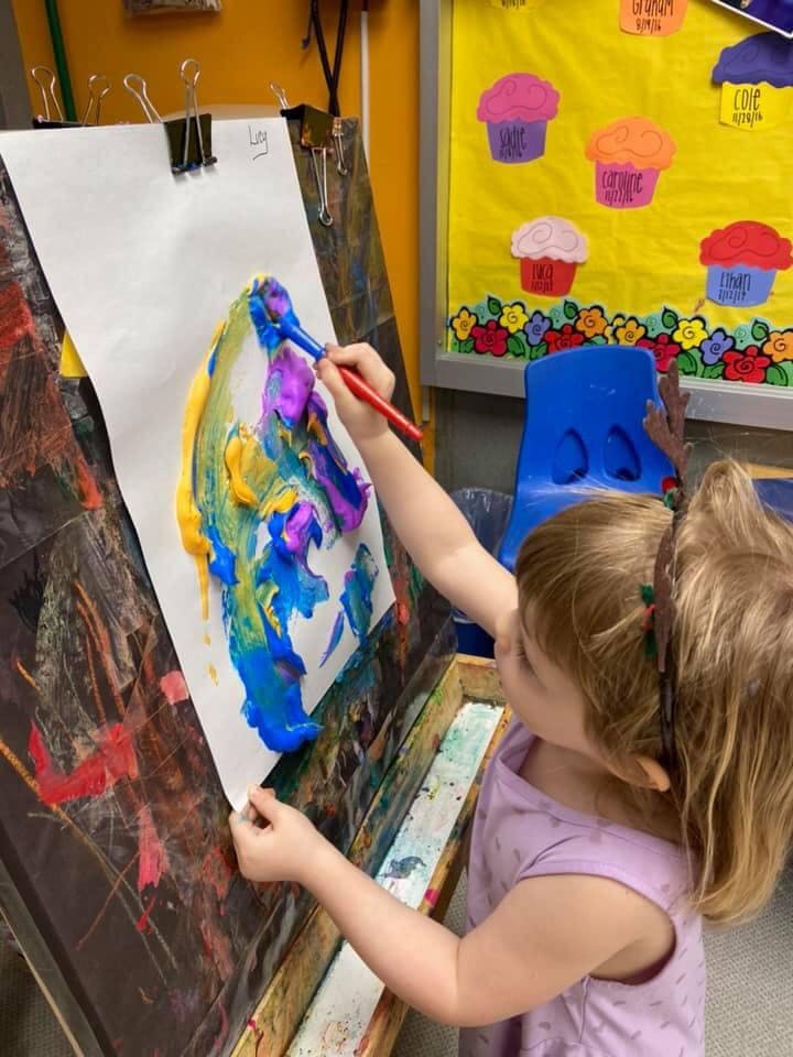 Child painting on an easel with thick colorful paint