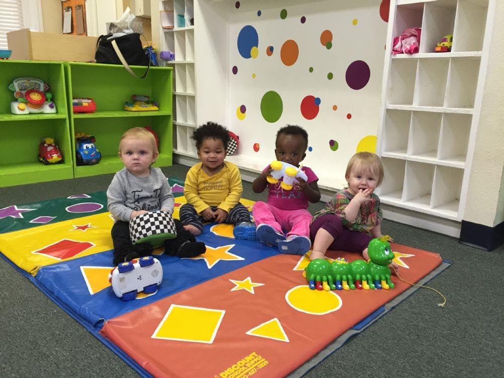 Four children playing with toys on a colorful mat in a classroom