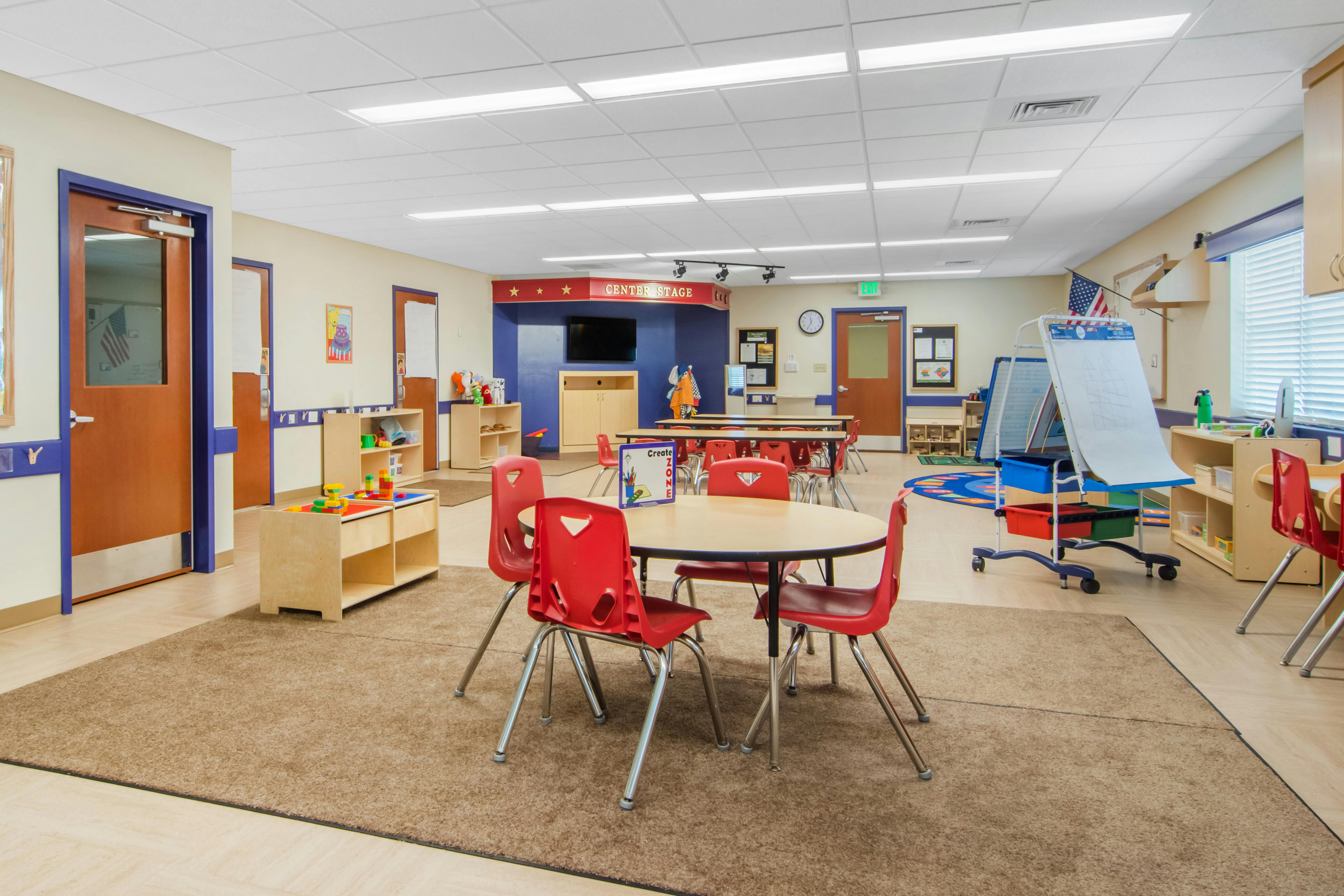 Classroom with small tables and chairs, a stage area, and various learning stations