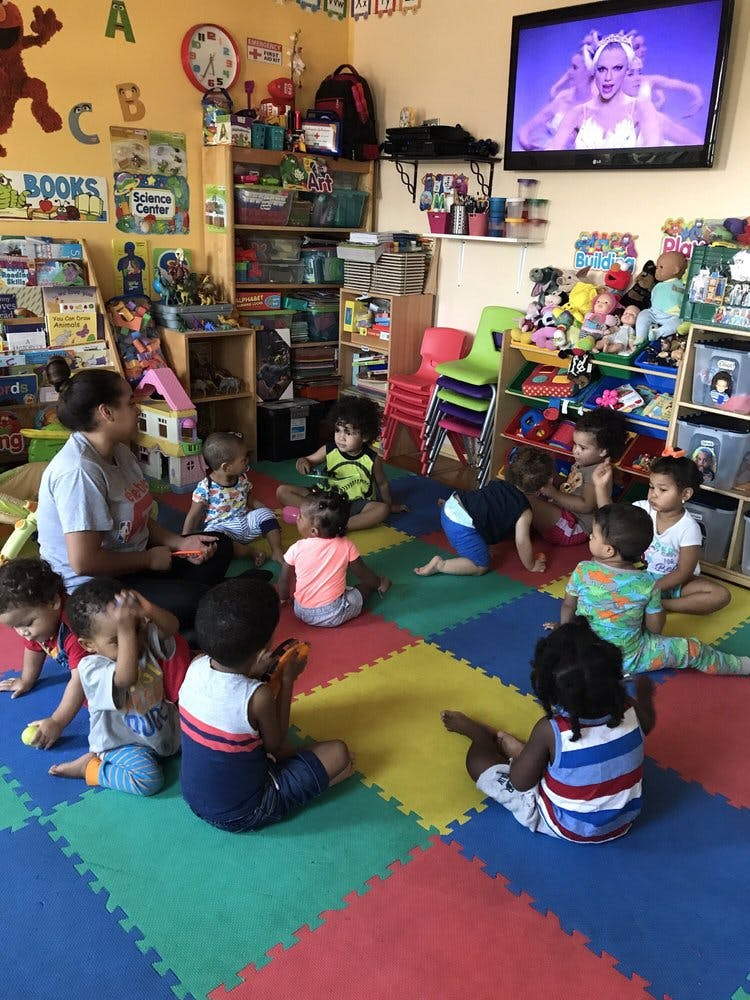 Adult and multiple children sitting on a colorful mat in a classroom