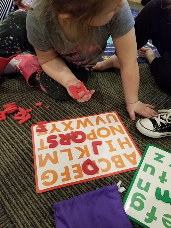 Child playing with red letter cutouts on an alphabet board
