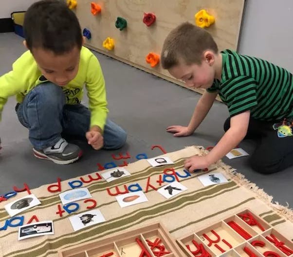 Two children kneeling on the floor, playing with letter cutouts and picture cards