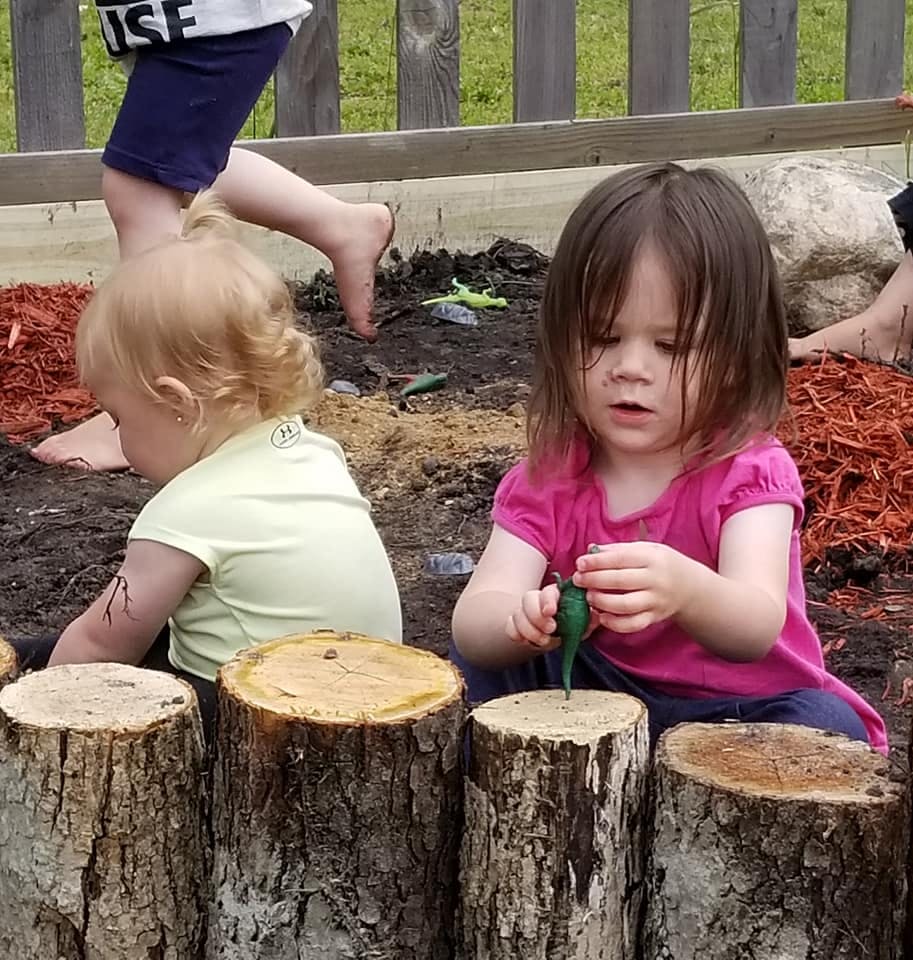 Two children playing in dirt with wood stumps