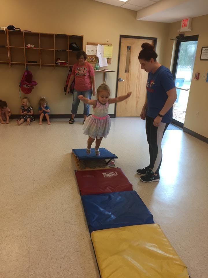 Child balancing on a blue mat with arms outstretched, person watching