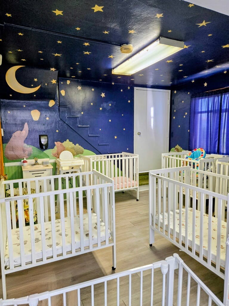 Cribs inside a childcare room with star-themed wall and ceiling murals