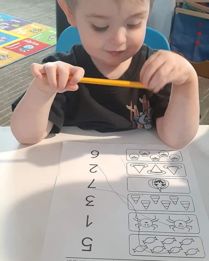 Child holding a yellow pencil over a number matching worksheet