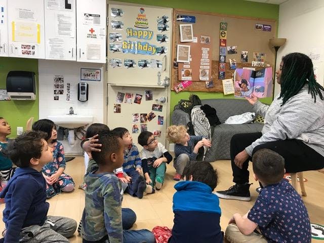 Adult reading a book to a group of children sitting on the floor