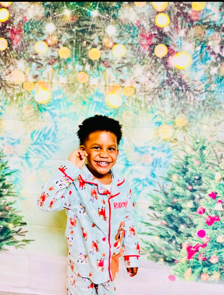 Child wearing holiday pajamas in front of a Christmas tree backdrop