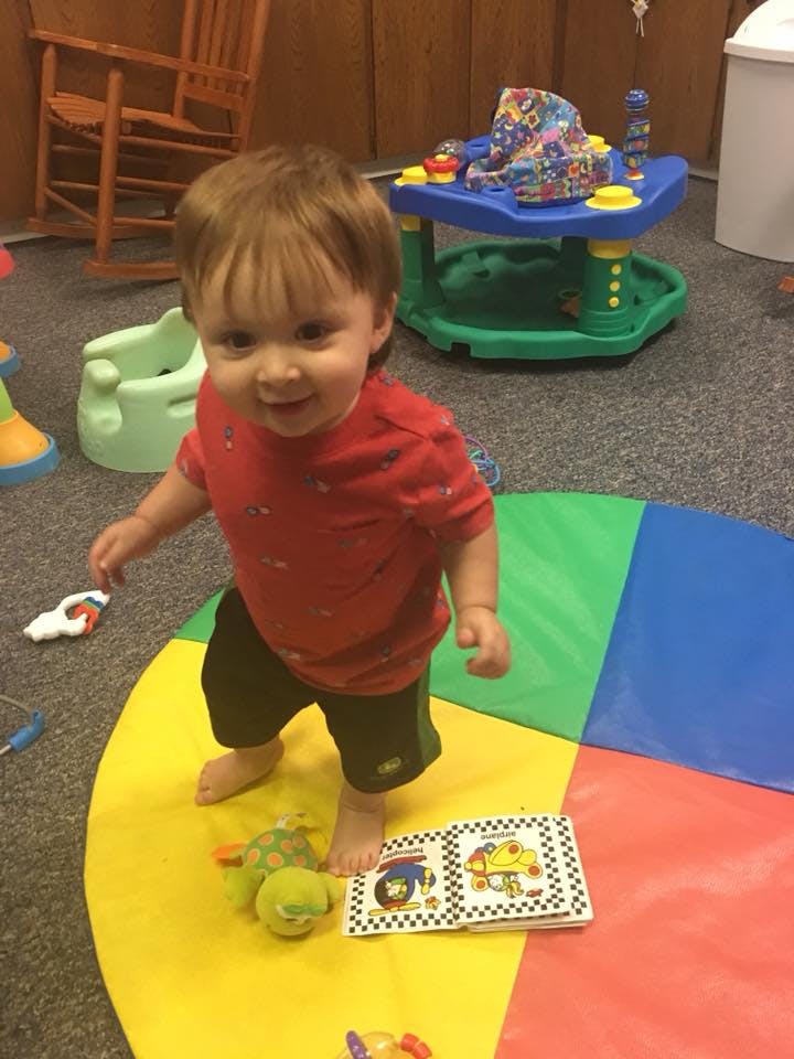 Child standing on a colorful playmat with a book and toy