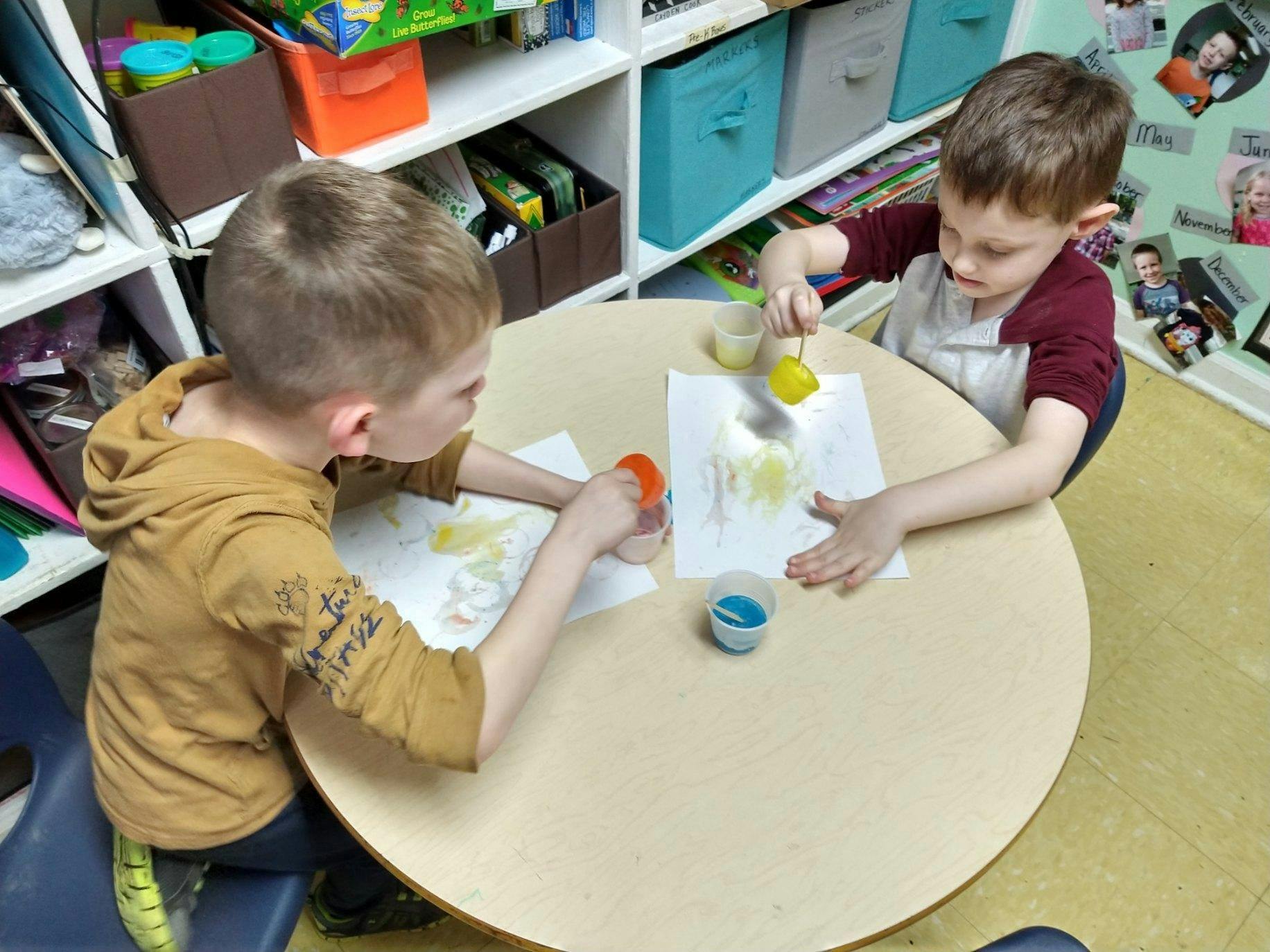 Two children painting at a round table