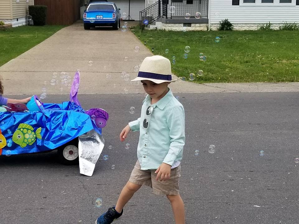 Child in a hat and sunglasses walking on a street with bubbles