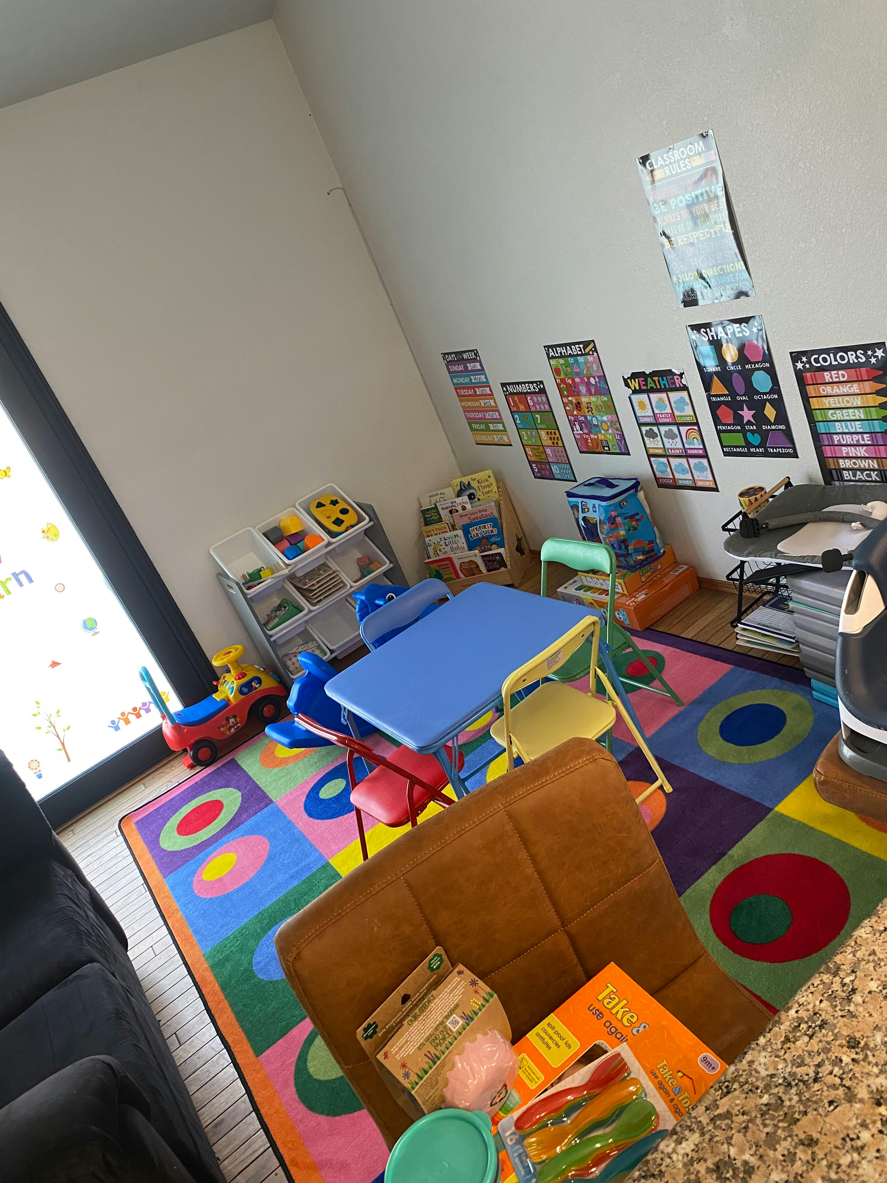 Classroom with colorful rug, small tables, chairs, and learning posters on the wall