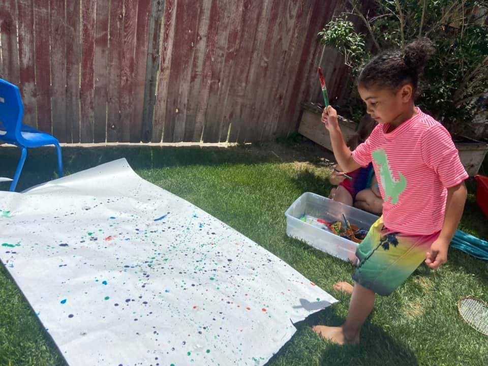 Child painting on a large sheet of paper outdoors