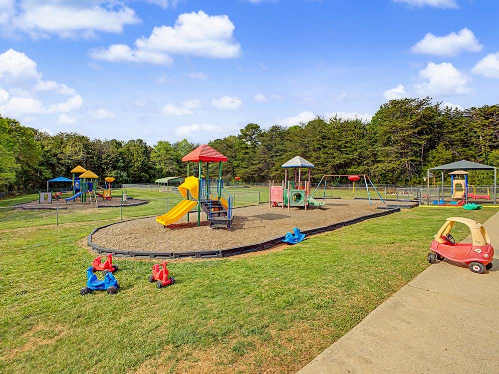 A fenced outdoor playground with multiple colorful play structures and ride-on toys