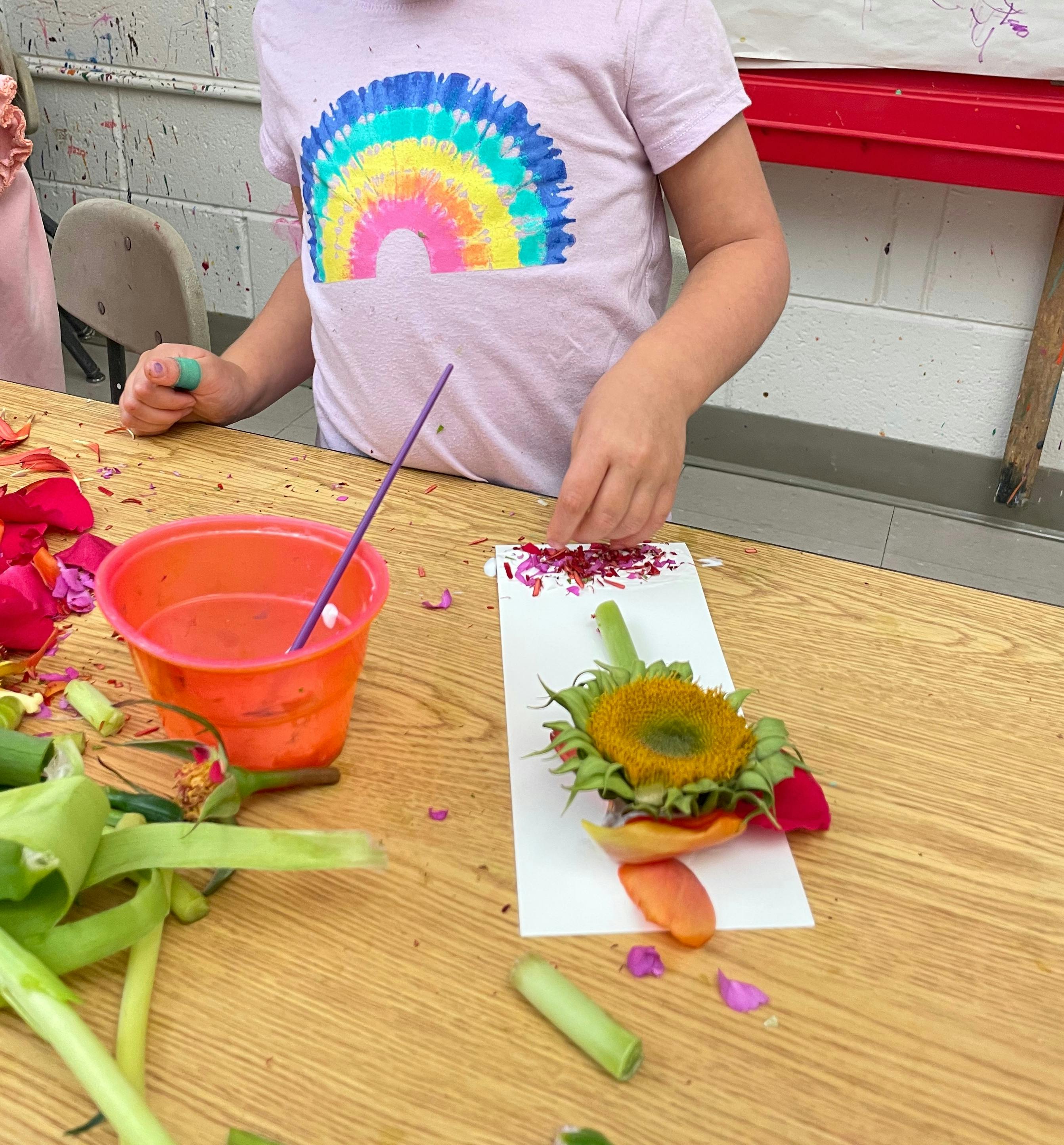 Child creating art with flower petals and a sunflower on a table