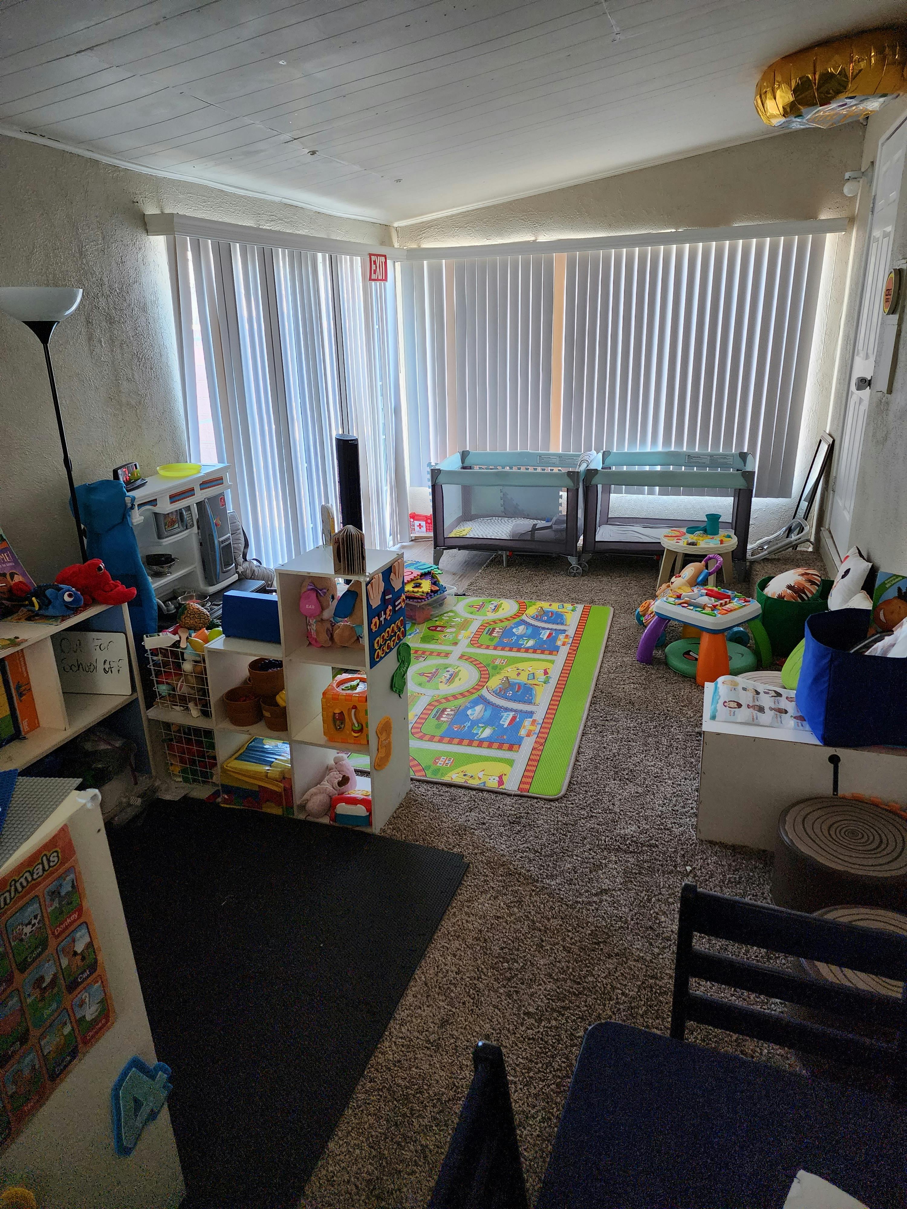Room with two cribs, a playmat, and shelves with toys