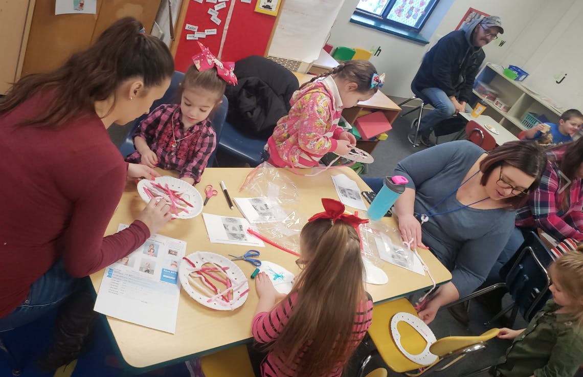 Adults and children doing crafts at tables in a classroom