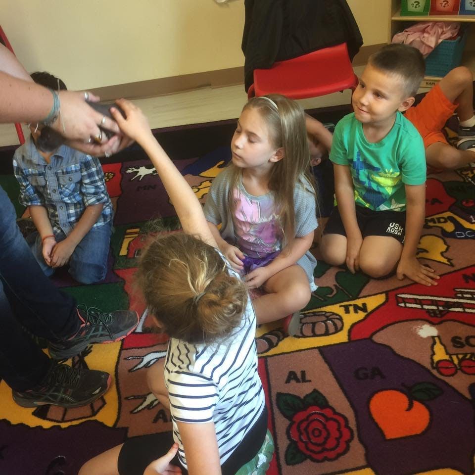 Children sitting on a rug, one child reaching out to touch an object