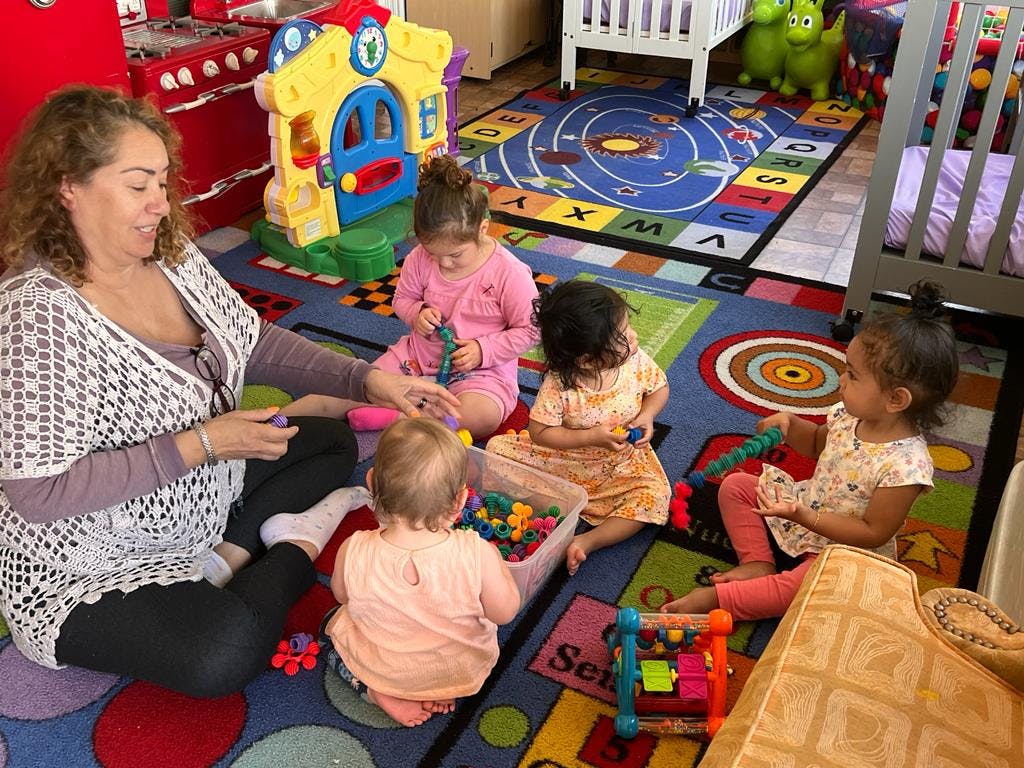 Person sitting on floor with four children playing with toys