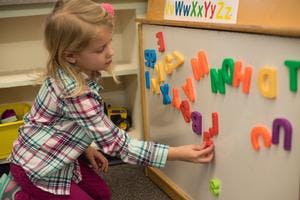 Child playing with magnetic letters on a whiteboard