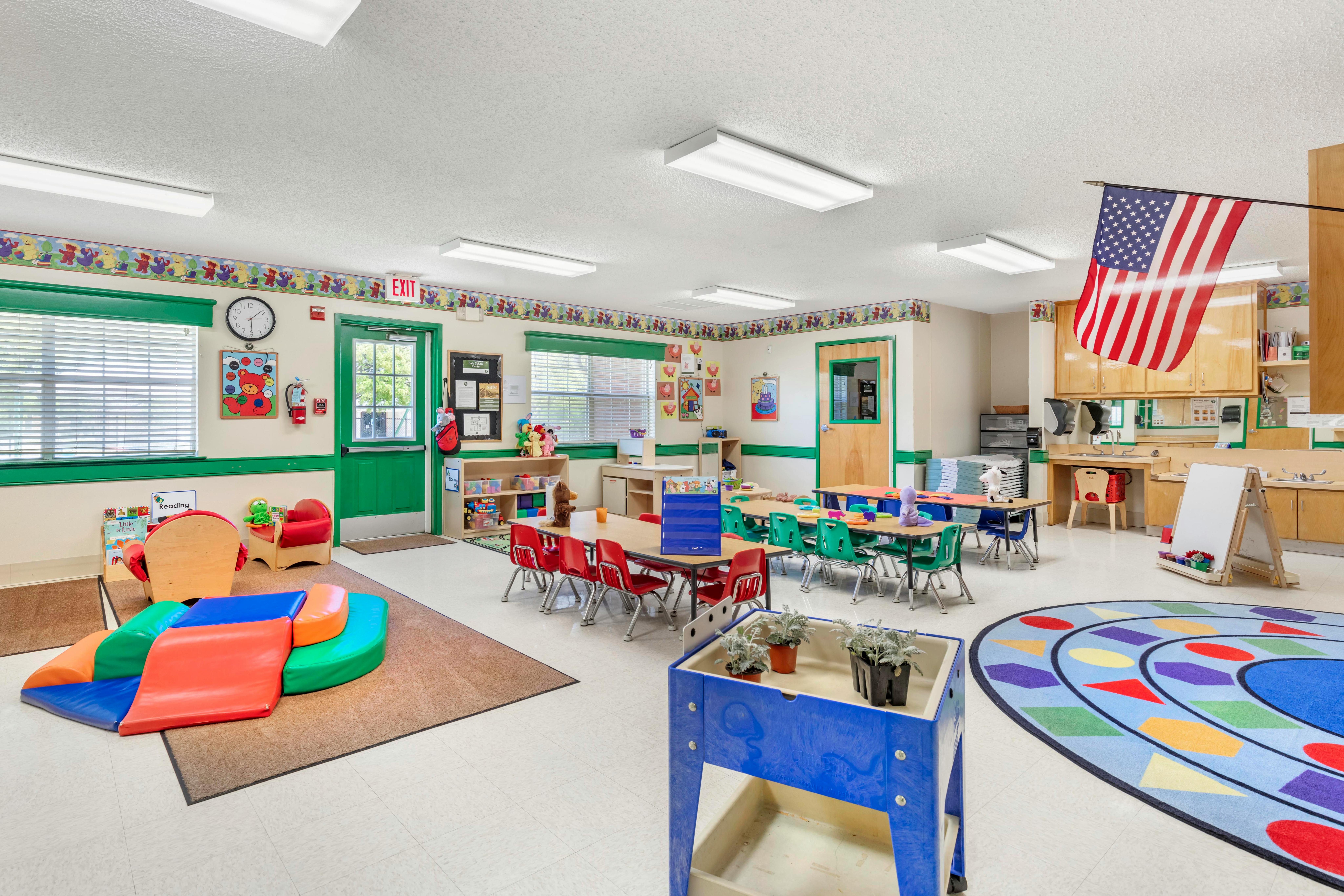 Colorful classroom with child-sized tables and chairs, play mats, and a US flag